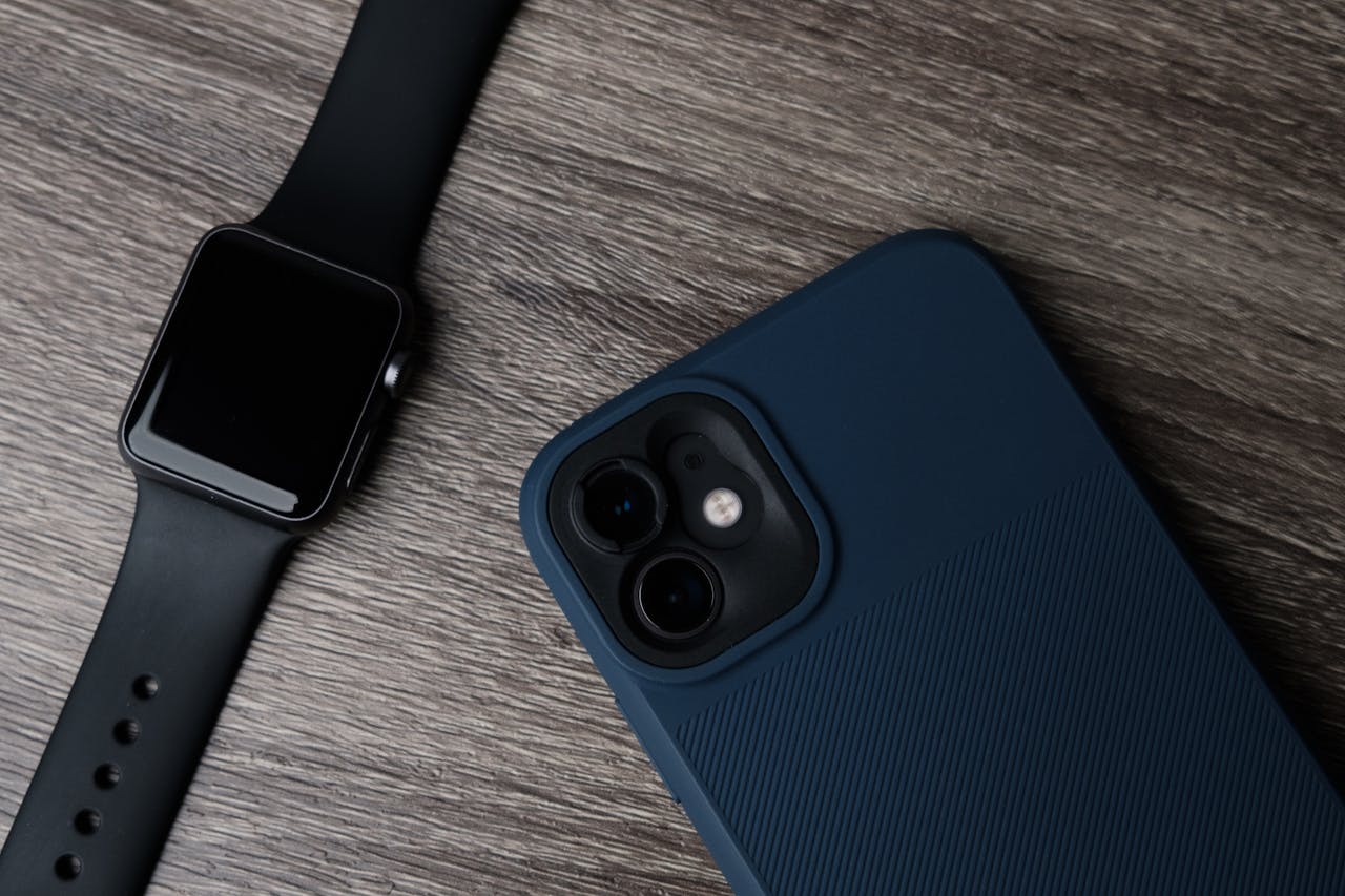 Close-up of a smartwatch and smartphone on a wooden surface, showcasing modern technology.